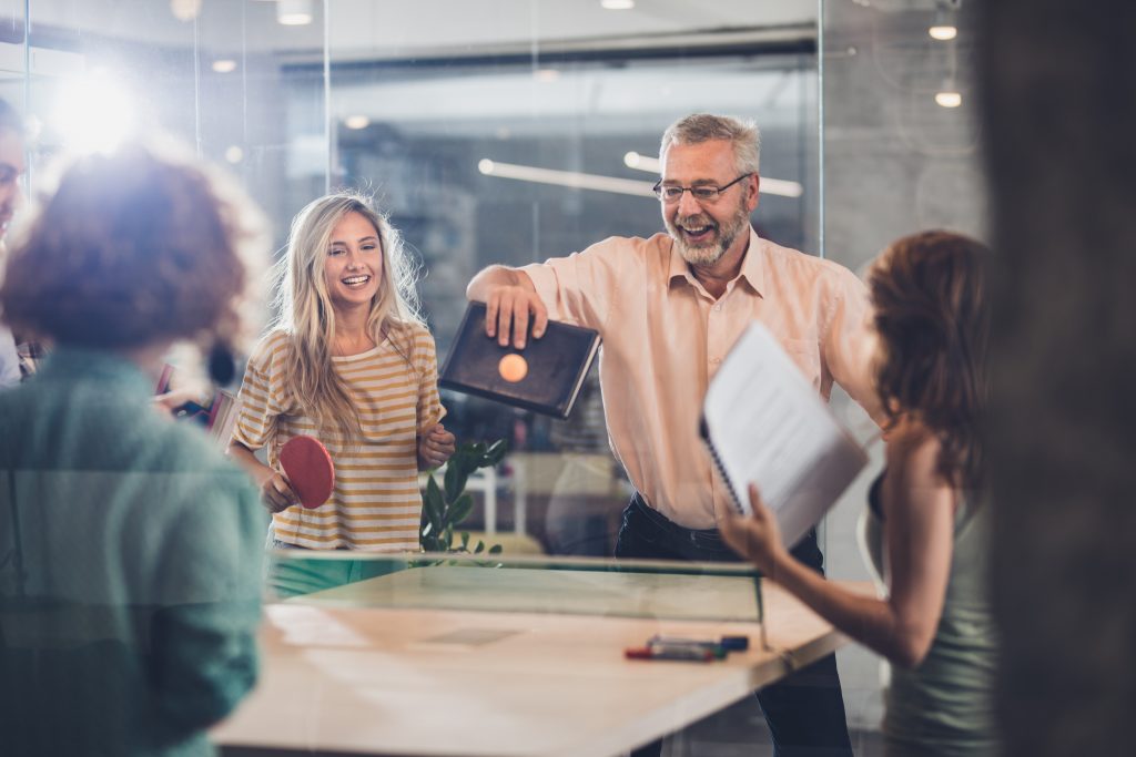 Senior man laughing while playing table tennis with students