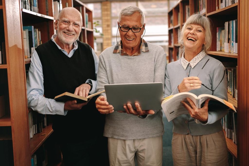 Three mature men and women in a library holding open books